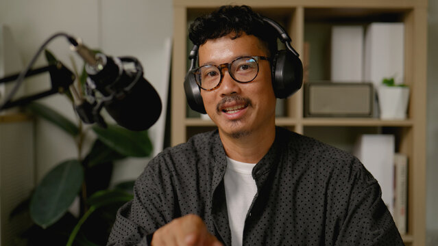 Asian man hosts and records a professional business podcast from his home studio.