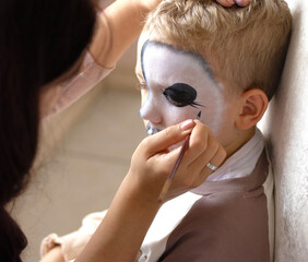 female hand with brush paints face of boy. Street makeup in style of Halloween. All Saints Day celebration or carnival cosplay competition. Halloween makeup, skulls, skeleton. Happy Halloween concept