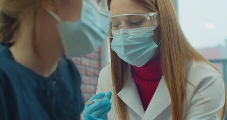 American doctor wearing face mask injects a covid-19 vaccine into the girl shoulder at home. concept of corona virus vaccine and treatment during pandemic. - Powered by Adobe
