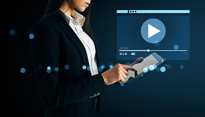 Businesswoman using tablet to stream video content on digital platform with futuristic background and glowing interface elements.