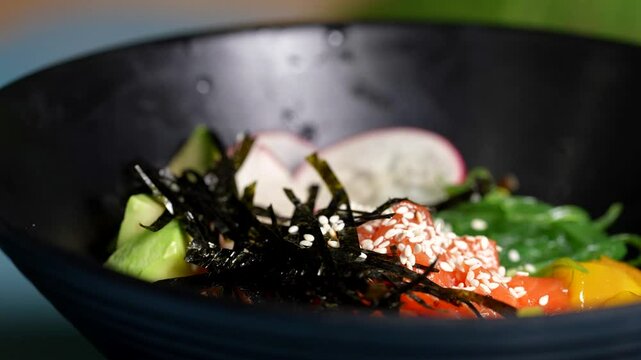 Close-up of poke bowl with avocado, salmon, cucumber, radish, seaweed, and sesame seeds on top.