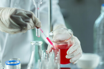 A gloved scientist carefullyDi Ding s a red liquid from a burette into a beaker.
