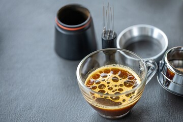 Close-up view of freshly brewed espresso shot in a glass cup with coffee accessories and tools on a dark surface, detailed barista equipment for coffee making