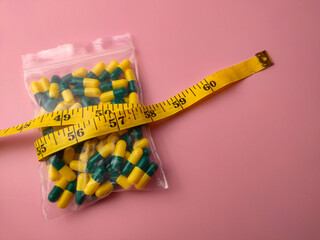 Closeup of a medicine pill package with measuring tape on a pink background