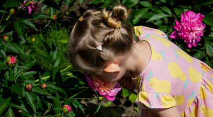 Naklejka premium little girl in the garden sniffing flowers. Selective focus