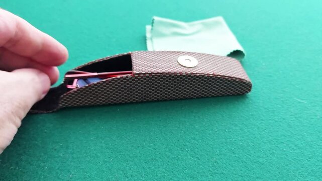 A hand carefully places sleek eyeglasses into a protective case on a vibrant green tabletop. The smooth motion and crisp contrast highlight elegance and practicality