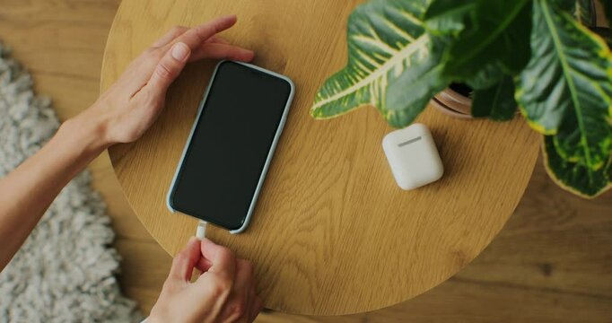 Top view. Woman plugging cable into a smartphone connector to charge.