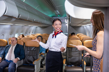 Flight attendant is welcoming and checking passenger boarding pass in business class and show the way to her seat for airplane flight and airline transportation