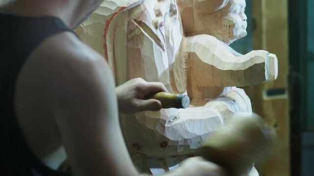 Skilled strong caucasian sculptor carving wooden virgin mary religious statue with mallet and chisel in workshop, showcasing creativity and craftsmanship in close up shot, slow motion