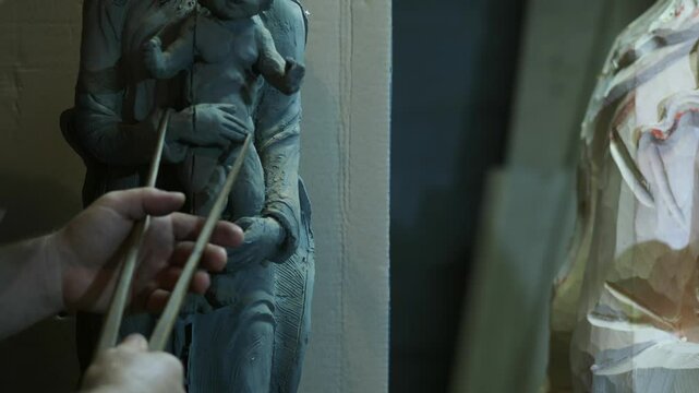 An artisan uses a caliper to precisely measure and compare proportions on a clay sculpture of the Madonna and Child, focusing on symmetry and accuracy during the modeling process, slow motion