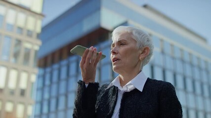 Senior woman using voice assistant on smartphone outdoors - Powered by Adobe