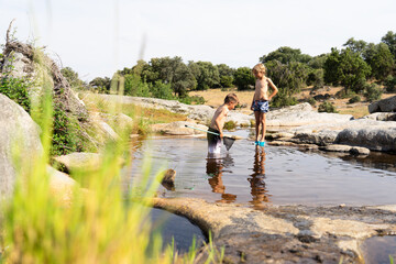 Children fishing with nets in a pond exploring nature during summer vacation