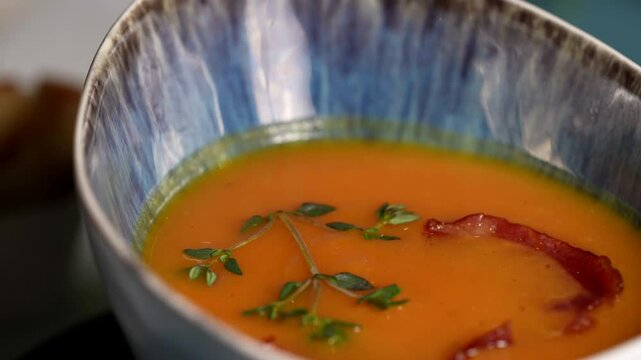 Close-up of tomato cream soup with herbs and crispy bacon, presented in a blue patterned ceramic bowl.