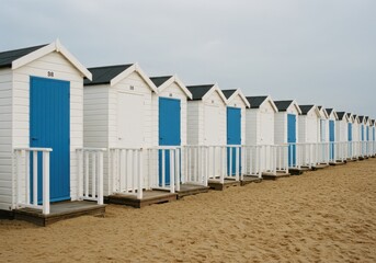Naklejka premium Row of beach huts with blue doors on a sandy beach under a cloudy sky
