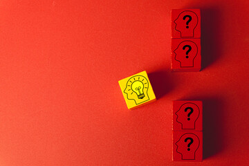 A yellow wooden block with a lightbulb idea icon stands out from red blocks with question marks.Concept for innovation,creativity,unique solutions,brainstorming,problem-solving,strategic thinking.