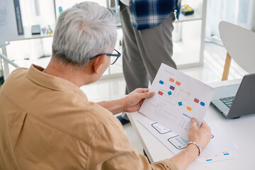 Senior programmer planning software development with flowchart and system process documentation at office