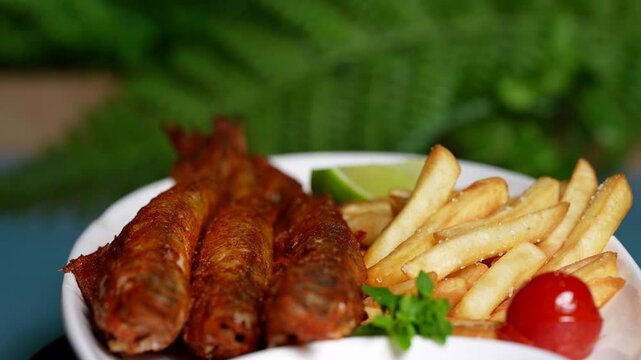 Plate with three fried fish, French fries, tomato, parsley and lime wedge, green background.