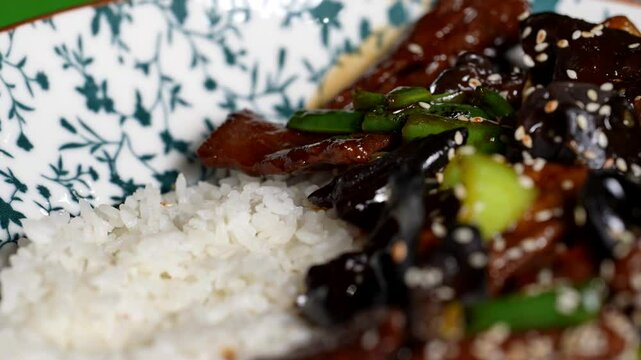 Close-up of glazed beef strips with wood ear mushrooms, green peppers, and rice on a floral plate.
