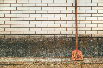 Old corroded shovel leaning on the white brick wall