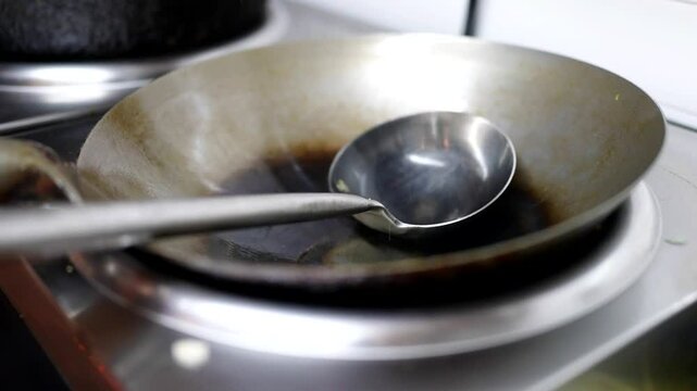 Stainless steel wok and ladle on stovetop, ready for cooking, with dark seasoning marks inside.