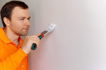 Man in Orange Shirt Painting Wall with Brush During Home Renovation