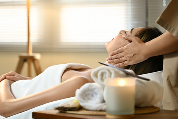 A woman is getting a massage while a massages therapist her head. The room is dimly lit and has candles and towels on the table
