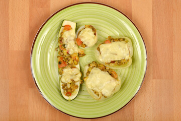 An overhead shot displays a green plate with baked zucchini, bell peppers, and onions stuffed with lentils and topped with melted cheese, set on a wooden surface