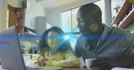 Image of light spots and trails over african american man and his daughter using laptop together