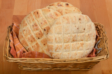 Three round flatbreads are arranged in a wicker basket with a checkered cloth on a wooden surface