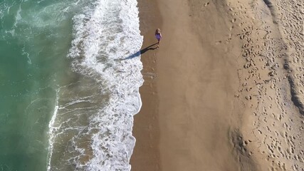 Slow motion aerial view of a gorgeous blonde woman walking on a beach. Sea waves washing sandy shoreline
