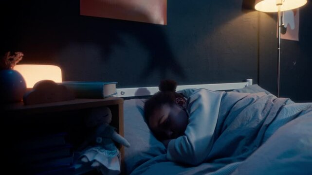 Little girl sleeping in bed in dark room at night with spooky hand silhouettes playing shadow game on wall under flickering light