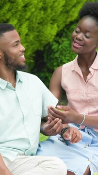 Vertical video: African American couple sharing smartphone after wrist grab in park to take selfie