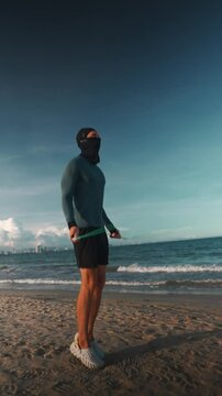 Man bodybuilder jumping rope at sea beach during sunset workout, Athlete training with jump rope by ocean shore at sunset for cardio exercise, vertical video 4k