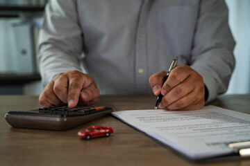 Insurance on paperwork assurance person gray shirt is working desk, using calculator and signing document with pen, with small red toy car nearby