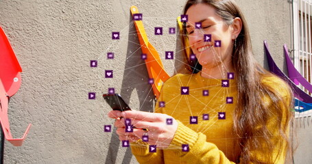 Image of globe of digital icons over caucasian woman using smartphone outdoors