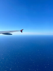 Naklejka premium Aerial View of Airplane Wing Over Turquoise Ocean – In-Flight Travel Photography