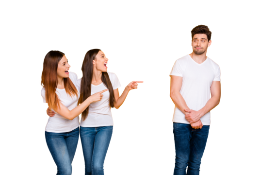 Portrait of confused person looking at funny girls teasing wearing white t-shirt denim jeans isolated over yellow background