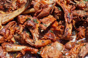 A close-up, top-down view of tender, roasted meat with bones and hints of herbs, submerged in a rich, savory sauce, suggesting a slow-cooked or traditional dish