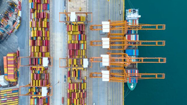 Aerial top down time lapse view of  large container cargo ship being unloaded by cranes and trucks in a commercial terminal port