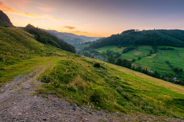 rural landscape in summer. carpathian range. village in the valley at dawn. forest and green meadow on the hill under red sky. scenic view of a countryside in mountains of ukraine