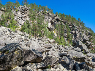 Large rocks and steep cliffs with trees growing on them on the shore of Lake Pizanets in Karelia in...