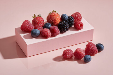 A pink rectangular supplement box, 40 x 28.5 cm in size, placed horizontally on a glossy white-pink reflective surface. The pink surface reflects the soft pink background. Mixed berries of various kin