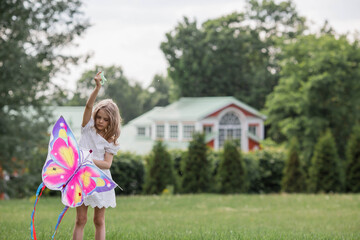 Naklejka premium Children in the summer park. A beautiful girl is flying a kite in the fresh air. Warm family moments or a conceptual image for spending time outdoors.