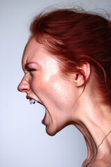 A red-haired woman with fair, freckled skin, captured in a dramatic side profile. Her eyes are tightly shut, eyebrows furrowed, and mouth wide open in a powerful scream