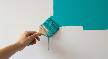 Person's hand with a paintbrush applying bright teal paint onto a plain white wall. Home renovation, interior design update, and do-it-yourself decorating concept.