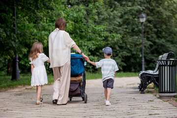 A family with three children. A mother with many children and toddlers in a summer park. Children are walking in the fresh air. Having many children and family values.