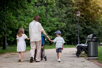 Obraz premium A family with three children. A mother with many children and toddlers in a summer park. Children are walking in the fresh air. Having many children and family values.