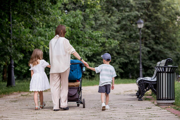 Obraz premium A family with three children. A mother with many children and toddlers in a summer park. Children are walking in the fresh air. Having many children and family values.