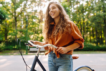 Young woman riding a bicycle in a green park. Cheerful woman enjoying weekend, bike ride at sunset....