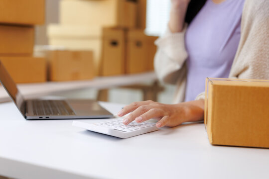 Online seller calculating shipping costs using calculator in warehouse